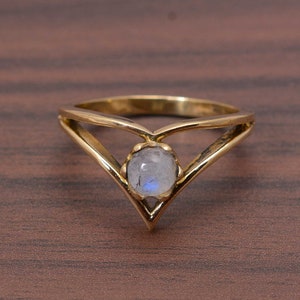 May include: A gold ring with a V-shaped band and a round moonstone gemstone in the centre.