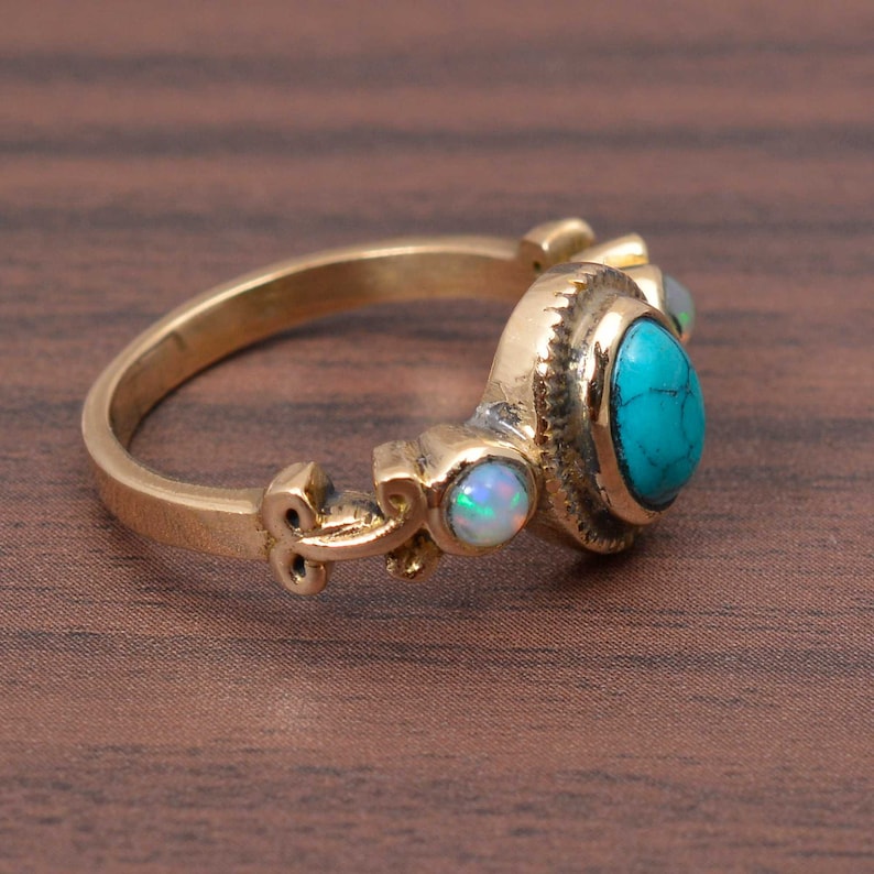 May include: A gold ring with a turquoise gemstone and two opal gemstones. The ring has a detailed design with intricate scrollwork.