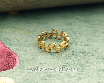 May include: A gold-colored ring with a leaf design. The ring is made of metal and features a repeating pattern of leaf shapes around the band. The ring is displayed on a green and pink surface. The text "JewelleryWorldDesign" is at the bottom.