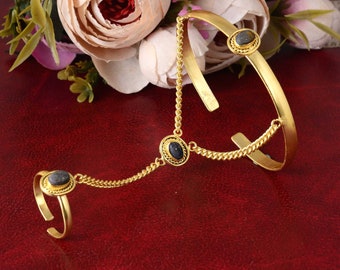 May include: Gold-toned hand chain bracelet with a ring and cuff design. The jewelry features three dark blue oval stones set in ornate bezels. Delicate chains connect the ring and cuff, creating a unique and elegant accessory.
