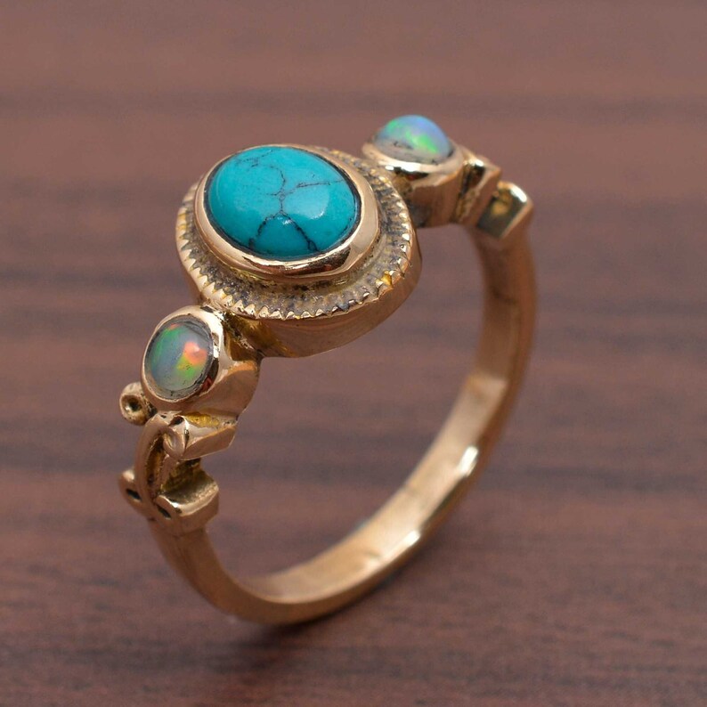 May include: A gold ring with three stones. The center stone is a turquoise oval cabochon. The two side stones are opals. The ring has a detailed design.
