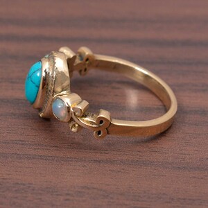 May include: A gold ring with a turquoise and opal gemstone setting. The ring has a delicate, ornate design.