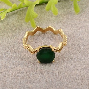 Op de afbeelding: Een gouden ring met een groene edelsteen. De ringband heeft een zigzagontwerp.