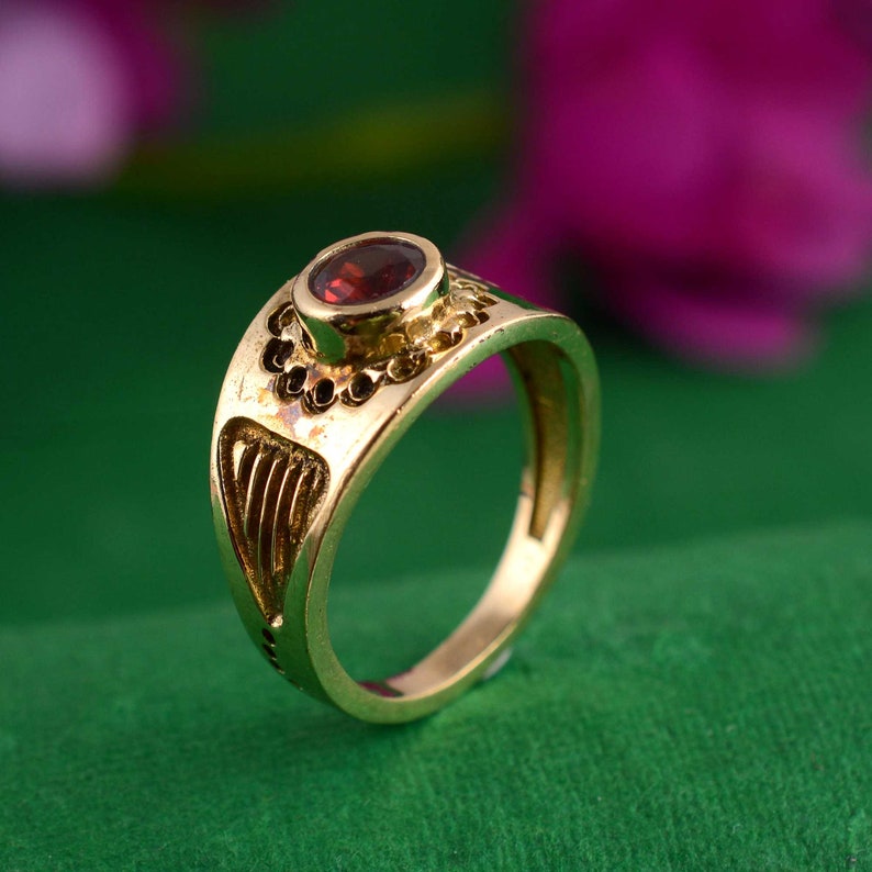 May include: A gold ring with a red gemstone set in the center. The ring has a detailed design with intricate carvings.