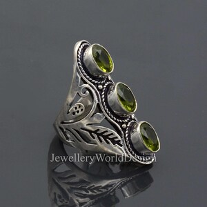 May include: A silver ring with an intricate floral design and three green gemstones. The ring is set against a grey background.