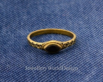 Puede incluir: Un anillo dorado con una piedra preciosa negra ovalada en el centro. La banda del anillo presenta un diseño intrincado y grabado. El anillo está sobre un fondo de mezclilla azul. El texto "Jewellery WorldDesign" es visible.