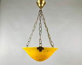 May include: A yellow glass pendant light fixture with a brass chain and a leaf design on the bottom.