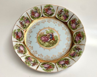 May include: A white porcelain plate with a gold rim and a blue and white floral design. The plate features a central image of a couple in a garden setting, surrounded by smaller images of couples in various poses.