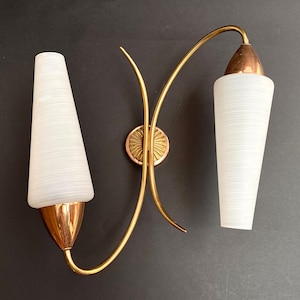 Puede incluir: Un par de apliques de pared doradas con pantallas de vidrio blanco esmerilado. Las apliques tienen un diseño moderno de mediados de siglo con brazos curvos.