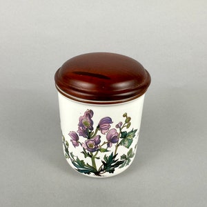 May include: White ceramic jar with a brown wooden lid. The jar features a floral design with purple and green flowers.