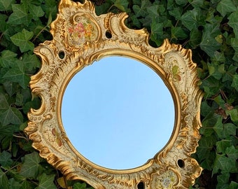 Könnte beinhalten: Ein runder Spiegel mit einem verzierten weißen und goldenen Rahmen. Der Rahmen hat einen abgenutzten Look und florale Details. Der Spiegel spiegelt einen blauen Himmel wider.