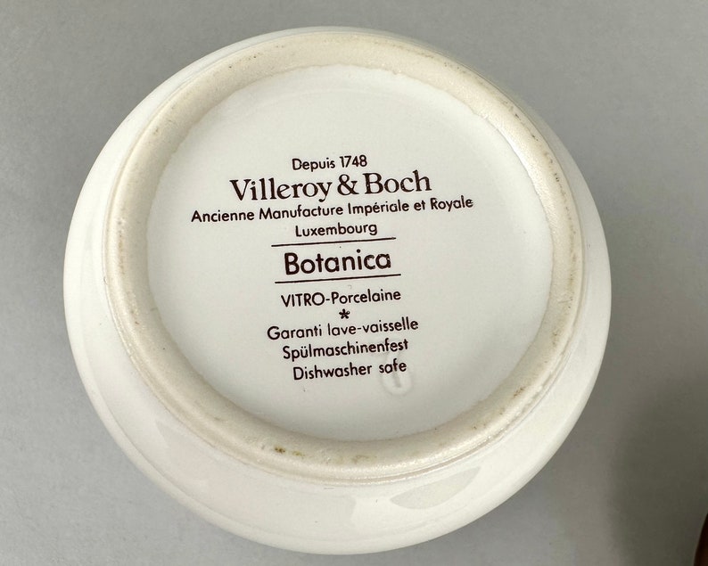 May include: Close-up of the bottom of a white ceramic bowl with brown text that reads "Depuis 1748 Villeroy & Boch Ancienne Manufacture Imp&eacute;riale et Royale Luxembourg Botanica VITRO-Porcelaine * Garanti lave-vaisselle Sp&uuml;lmaschinenfest Dishwasher safe".