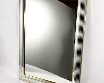 Könnte beinhalten: Ein großer rechteckiger Spiegel mit einem gold- und silberfarbenen, abgeschrägten Rahmen. Der Rahmen besteht aus einer Reihe schmaler, vertikaler Spiegelstreifen, die ein geometrisches Muster bilden.