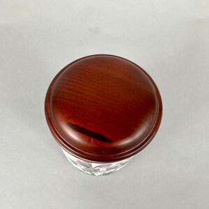 May include: A wooden lid with a dark brown finish. The lid is round and has a smooth surface.