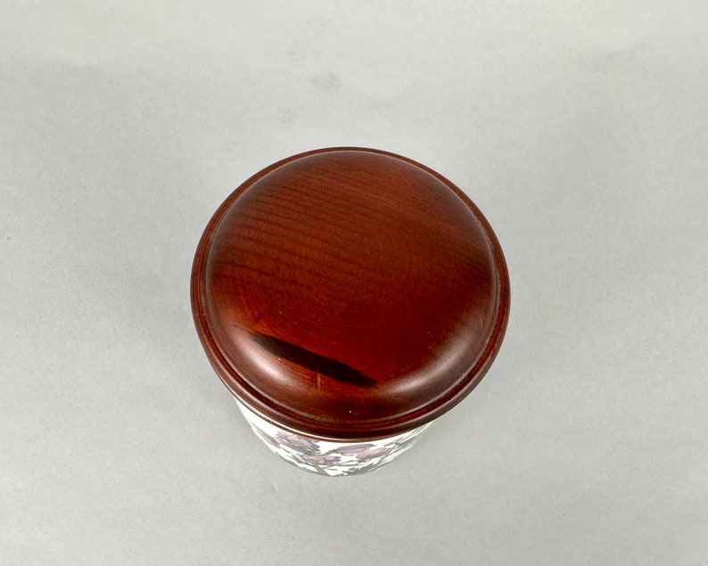 May include: A wooden lid with a dark brown finish. The lid is round and has a smooth surface.
