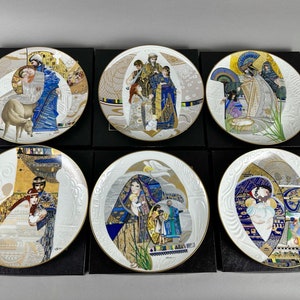 May include: Set of six white porcelain plates with gold trim, each featuring a different scene from the Nativity story. The plates are decorated with intricate details and vibrant colours, including blue, gold, and red.