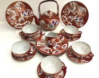 May include: A red and gold Japanese tea set with a teapot, creamer, and six cups and saucers. The set features intricate floral and figure designs.