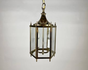 May include: A brass and glass pendant light fixture with a hexagonal shape. The glass panels have a starburst design etched into them. The light fixture has a chain and a hook for hanging.
