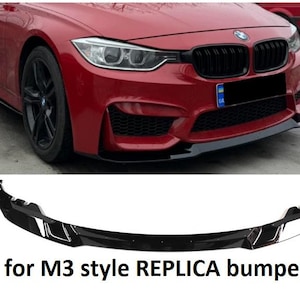 May include: A black plastic car bumper for a BMW 3 Series. The bumper has a sporty design with a black grille and a black lip spoiler. The text "for M3 style REPLICA bumper" is printed on the bottom of the image.