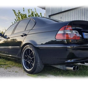May include: A black BMW 3 series sedan with aftermarket wheels and a rear diffuser. The car has dual exhaust tips and a black license plate.