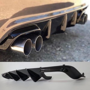 Op de afbeelding: Zwarte achterdiffuser met vier vinnen voor een auto. De diffuser heeft een glanzende afwerking en is ontworpen om de aerodynamica te verbeteren.