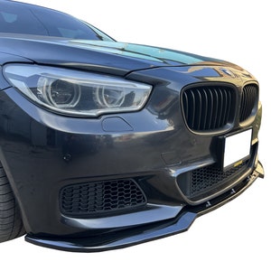 Puede incluir: Un spoiler de parachoques delantero negro para un coche BMW Serie 5. El spoiler está hecho de plástico negro brillante y tiene un diseño elegante y aerodinámico.