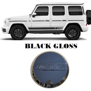 May include: Black gloss gas cap with a chrome AMG logo. The cap is round and has a black background.