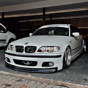 Può includere: Una berlina BMW Serie 3 bianca con un paraurti anteriore nero e cerchi neri. L'auto ha un adesivo "1300.nl" sul parabrezza.