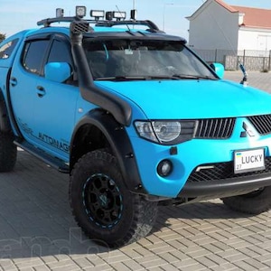 May include: A bright blue pickup truck with black fender flares and a black roof rack. The truck has a black grille with a chrome Mitsubishi emblem and a black bumper. The truck has a number plate that reads "LUCKY 27".