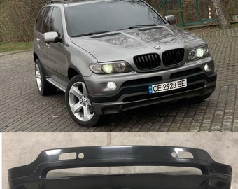May include: A black plastic car bumper with a large opening in the center and two smaller openings on either side. The bumper is designed to fit a BMW X5.