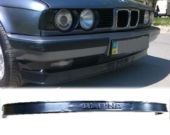 Può includere: Paraurti anteriore nero con logo "ALPINA" nero per un'auto. Il paraurti ha un design liscio e curvo e un sottile spoiler a labbro.