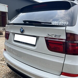 Könnte beinhalten: Ein weißer BMW X5 SUV mit einem schwarzen Heckspoiler und einem "TOP-CARS SLAVUTA" Aufkleber auf der Heckscheibe.