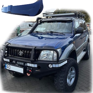 Pode incluir: Um Toyota Land Cruiser azul com um rack de teto preto e um para-choque dianteiro preto. O carro tem uma placa de matrícula que diz "AO".