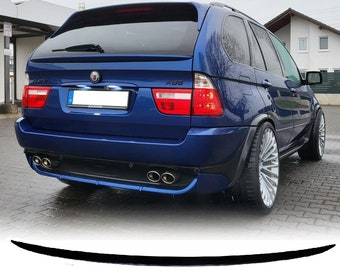 May include: A blue BMW X5 with a black rear spoiler. The car has a black rear bumper with dual exhaust pipes and a license plate holder. The car is parked on a paved surface.