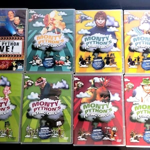 May include: A collection of eight DVD cases featuring the comedy group Monty Python. The cases have colorful designs with the title "Monty Python's Flying Circus" and "Monty Python Live!" The DVDs are in plastic cases.