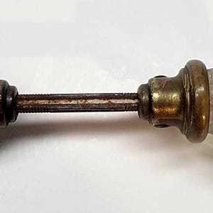 May include: Antique door knob with two aquamarine glass knobs and brass hardware. The glass knobs have a ribbed design and are connected by a metal rod. The hardware shows signs of age and wear.