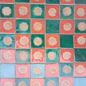 Op de afbeelding: Een schaakbordpatroon van groene, rode en blauwe tegels met een bloemmotief. Elke tegel heeft een reliëf, wit bloemmotief.