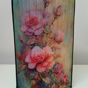 May include: A framed watercolor painting of pink roses with green leaves on a textured background.