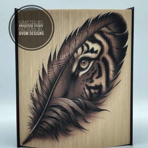 May include: A wooden art piece with a tiger eye and feather design. The artwork is made from layered wood, creating a 3D effect. It has a dark brown frame and the text "CRAFTED BY BRIGHTSIDE STUDIO PATTERN BY BVDM DESIGNS".