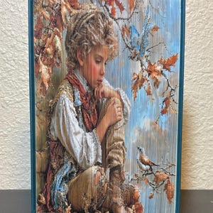 Puede incluir: Una escultura de libro plegado que presenta una imagen detallada de una persona con cabello rizado sentada entre hojas de otoño y ramas. La persona viste una camisa blanca y un chaleco estampado, mirando a un pequeño pájaro en una rama.