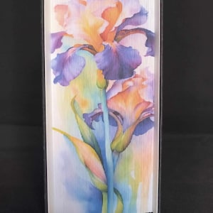 May include: A book with a colorful watercolor painting of an iris flower on the cover. The flower is a vibrant mix of purple, orange, and yellow.