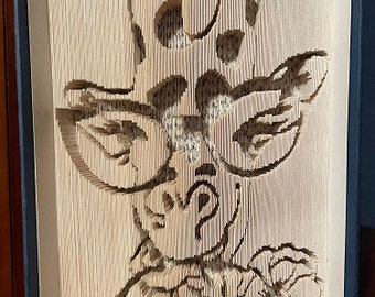 Könnte beinhalten: Eine Buchkunstskulptur einer Giraffe, die einen Hut und eine Brille trägt, mit einer Blume im Maul. Die Skulptur ist aus gefaltetem Papier gefertigt und ein einzigartiges und dekoratives Stück.