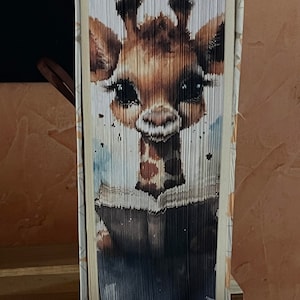 Op de afbeelding: Decoratief boek met een girafontwerp. De giraf, in bruine en witte tinten, leest een boek. De pagina's van het boek zijn gevouwen om de afbeelding van de giraf te creëren. Het boek heeft een patroon op de kaft.