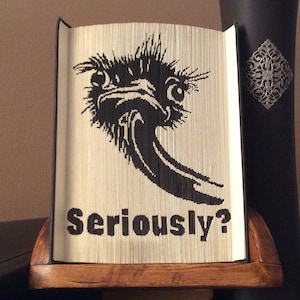 May include: A book art sculpture of an ostrich with the text "Seriously?" printed below. The sculpture is displayed on a wooden stand.