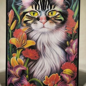 May include: A black and white tabby cat with green eyes sits in a field of colourful flowers. The flowers are red, yellow, purple, and orange. The cat is looking directly at the viewer.