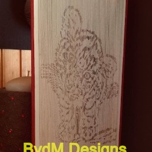 Puede incluir: Una escultura de arte de libro de la cara de un tigre, creada doblando las páginas de un libro. La escultura está sobre una superficie de madera y tiene un lomo rojo. El texto "BvdM Designs" está en la parte inferior de la escultura.