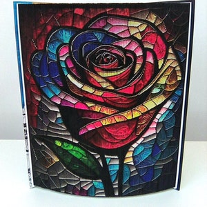 May include: A colorful stained glass rose with a green stem and leaves. The rose is made of many small pieces of glass in shades of red, pink, blue, yellow, and green.