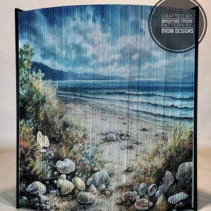 Könnte beinhalten: Ein gebogener Raumteiler aus dünnen Holzlatten, bemalt mit einer Strandszene. Die Szene zeigt einen Sandstrand, blaue Meereswellen, einen bewölkten Himmel und eine felsige Küste. Der Text "CRAFTED BY BRIGHT SIDE STUDIO PATTERN BY BVDM DESIGNS" ist auf dem Raumteiler aufgedruckt.