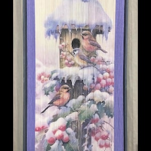 May include: A purple and white book art sculpture of a birdhouse with birds perched on the edge. The birdhouse is covered in snow and the background is a snowy forest scene.