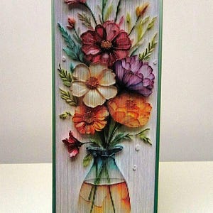 May include: A book sculpture of a vase with a bouquet of colorful flowers. The flowers are red, pink, white, purple, and orange. The vase is clear glass with a blue tint.